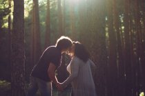 Man kissing pregnant woman in sunny forest. Horizontal outdoors shot. — Stock Photo