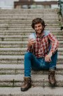 Bearded man in smiling while looking in smartphone on street steps — Stock Photo