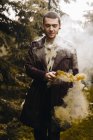 Ritratto di giovane uomo in posa con candela fumogena nel bosco — Foto stock