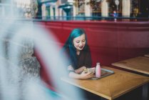 Retrato de menina com cabelo azul sentado na mesa do café e usando smartphone — Fotografia de Stock