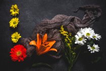 Modello floreale creativo con diversi fiori colorati e tessuto sguardo marrone sulla superficie scura — Foto stock