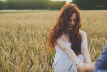 Портрет рыжеволосой девушки на ржаном поле, держащей парней за руки и смотрящей вниз — стоковое фото