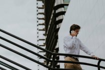 Low angle view of businessman in white shirt standing at stairs passage and talking on smartphone over business buildings glass facade — Stock Photo