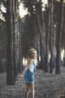 Счастливый ребенок позирует в лесу и смотрит через плечо на камеру, показывая язык — стоковое фото
