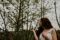 Чувственная девушка в белом платье касается стебля с листьями — стоковое фото