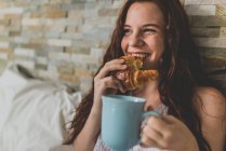 Mädchen isst Croissant mit Tasse Kaffee im Bett — Stockfoto