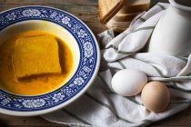 Hochwinkelige Ansicht eines verzierten Tellers mit Brotscheibe, die in zertrümmerten Eiern auf einem Tisch mit Handtuch und Eiern liegt — Stockfoto