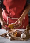 Seção intermediária de fatia feminina segurando de bolo caseiro sobre papel de padaria com colher de anis estrelas, bolo e ovo na mesa de cozinha rústica branca — Fotografia de Stock