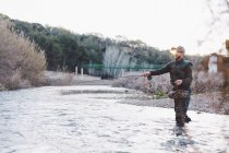 Вид сбоку на человека, стоящего в реке и рыбачащего — стоковое фото