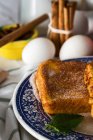 Vue rapprochée des toasts sucrés sur assiette ornée au-dessus des œufs et des bâtonnets de cannelle en toile de fond — Photo de stock