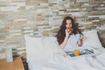 Young red-haired woman eating breakfast in bed — Stock Photo