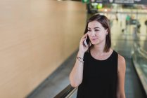Porträt einer jungen Frau, die sich auf der Rolltreppe bewegt und mit dem Smartphone spricht — Stockfoto