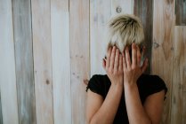 Girl with short blonde hair hiding face with hands — Stock Photo