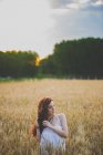 Retrato de menina com longos cabelos vermelhos curvilíneos posando no campo de centeio ao pôr do sol — Fotografia de Stock