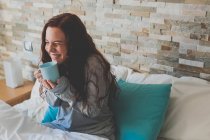 Girl sitting in bed and holding blue mug — Stock Photo