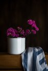 Натюрморт з фіолетовими квітами в білому горщику на столі з рушником — стокове фото