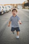 Ritratto di ragazzo carino in pantaloncini che corre felicemente verso la macchina fotografica su strada . — Foto stock