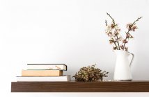 Fresh cut blooming sprigs in vase on shelf with books — Stock Photo