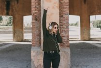 Дівчина в навушниках позує з піднятою рукою — стокове фото