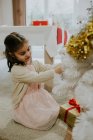 Portrait of child girl sitting on ground and decorating white Christmas tree. — Stock Photo