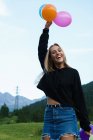 Mujer rubia sonriente posando con globos en la naturaleza - foto de stock