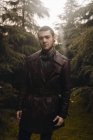 Ritratto di uomo che indossa un cappotto di pelle in posa tra i boschi e guarda la macchina fotografica — Foto stock