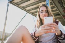 Low angle view of girl using smartphone at street scene — Stock Photo