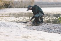 Вид сбоку человека, стоящего на коленях у реки и ловящего удочку — стоковое фото