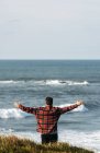 Rear view of man standing with outstretched hands on seashore — Stock Photo