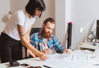 Portrait of male and female architects discussing blueprints in office — Stock Photo