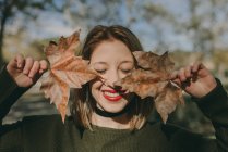 Девушка с закрытыми глазами держит кленовые листья возле лица — стоковое фото