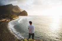 Male standing and looking at cliffs and sea shore, back view. — Stock Photo