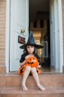 Girl in witch costume with pumpkin over open door — Stock Photo