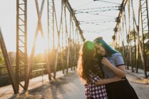 Friends hugging on bridge at sunset — Stock Photo