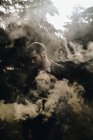 Portrait of man posing in color smoke among woods — Stock Photo