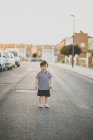 Retrato de lindo niño sonriendo a la cámara mientras está de pie en el camino de asfalto en el suburbio - foto de stock