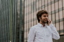 Porträt eines brünetten Geschäftsmannes im weißen Hemd, der in der Innenstadt mit dem Smartphone spricht — Stockfoto