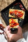 Sopra vista di mano tenendo cracker con pomodori secchi ove teglia sul tavolo — Foto stock