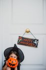 Menina em traje de bruxa escondendo rosto com saco de abóbora — Fotografia de Stock