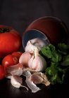 Gousses d'ail fraîches avec tomates fraîches et persil sur fond sombre avec pot — Photo de stock