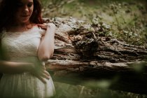 Chica de la cosecha en vestido blanco apoyado en el árbol en el bosque - foto de stock