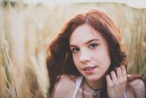Крупный план портрета молодой рыжей девушки, сидящей на ржаном поле и смотрящей в камеру — стоковое фото
