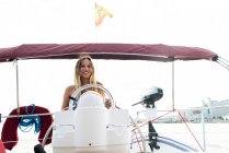 Вид спереди девушки, стоящей за штурвалом на палубе яхты в солнечный день — стоковое фото