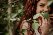 Retrato de chica pelirroja mirando a la cámara a través de hojas verdes - foto de stock