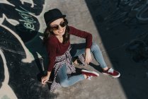 De arriba tiro de joven elegante hembra en skatepark sonriendo amplia en la luz del sol. - foto de stock