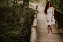 Chica jengibre alegre posando en vestido blanco en el puente de madera - foto de stock