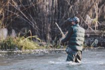 Rear view of man standing in country river and fishing with rod — Stock Photo