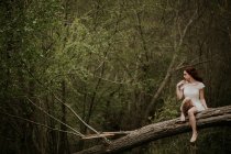 Рыжая девушка в белом платье позирует на упавшем дереве — стоковое фото