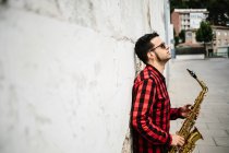 Jazzer lehnt sich an Wand und hält Saxofon — Stockfoto