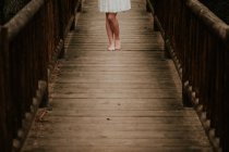 Section basse de fille en robe blanche posant sur un pont en bois — Photo de stock